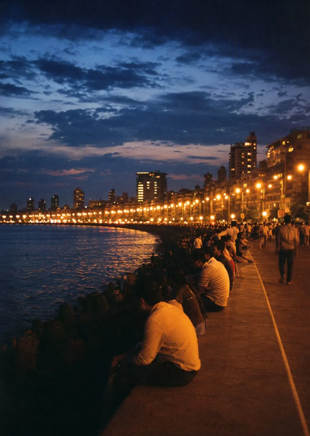 People sitting beside Marine Drive as the lights come on